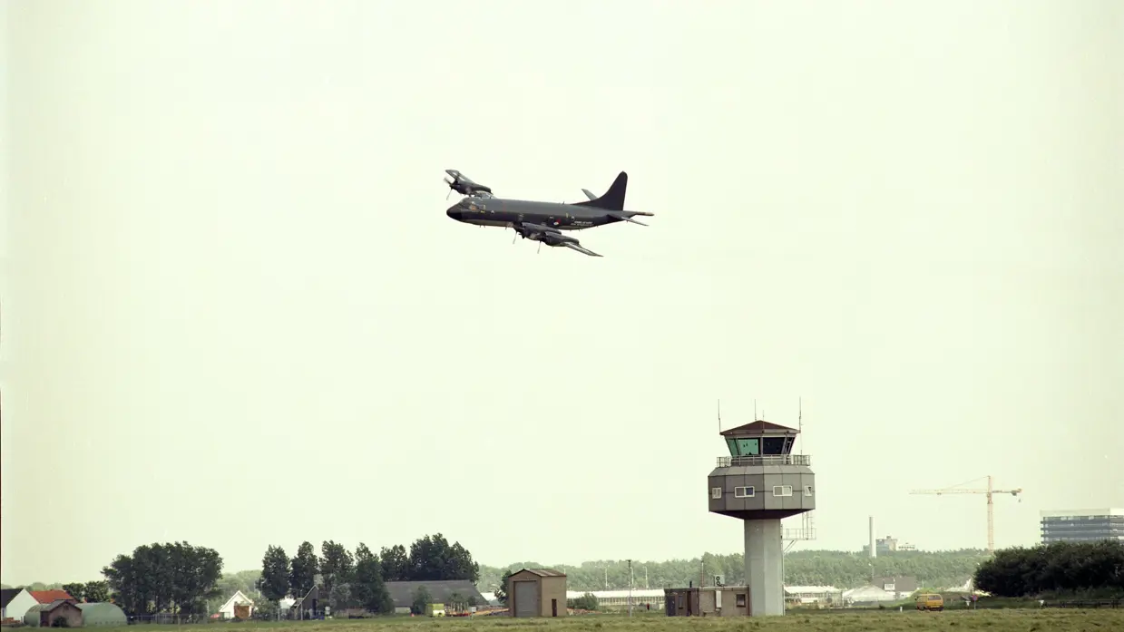 Een P3-C Orion vliegt boven de verkeerstoren van Marinevliegkamp Valkenburg.