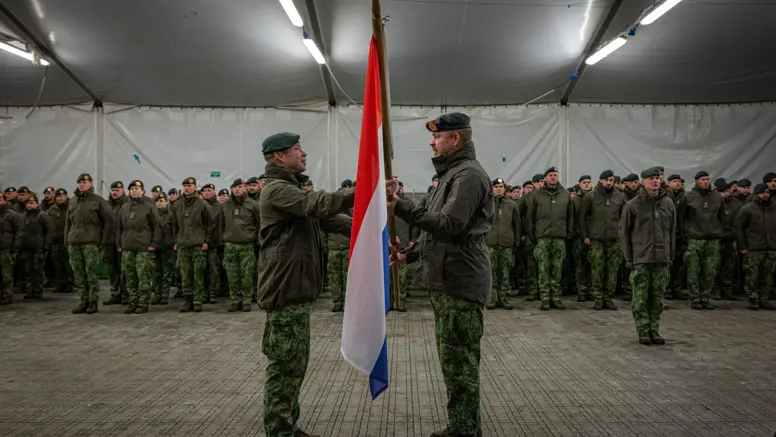 Alt-tekst: 2 militairen staan tegenover elkaar en houden Nederlandse vlag vast. 