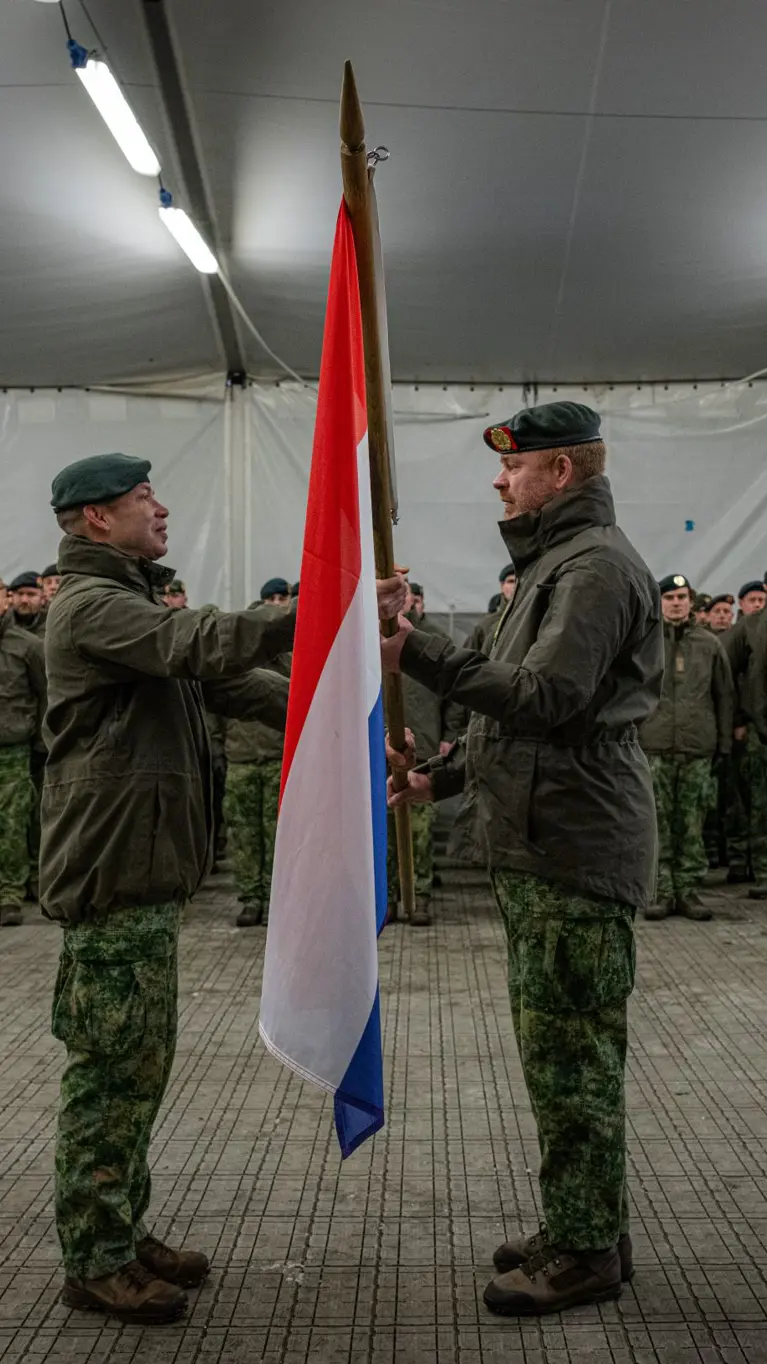 Alt-tekst: 2 militairen staan tegenover elkaar en houden Nederlandse vlag vast. 