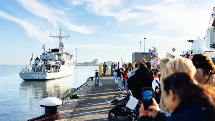 Zr.Ms. Willemstad gaat afmeren aan een kade waarop vrienden en familie de opvarende welkom heten. 
