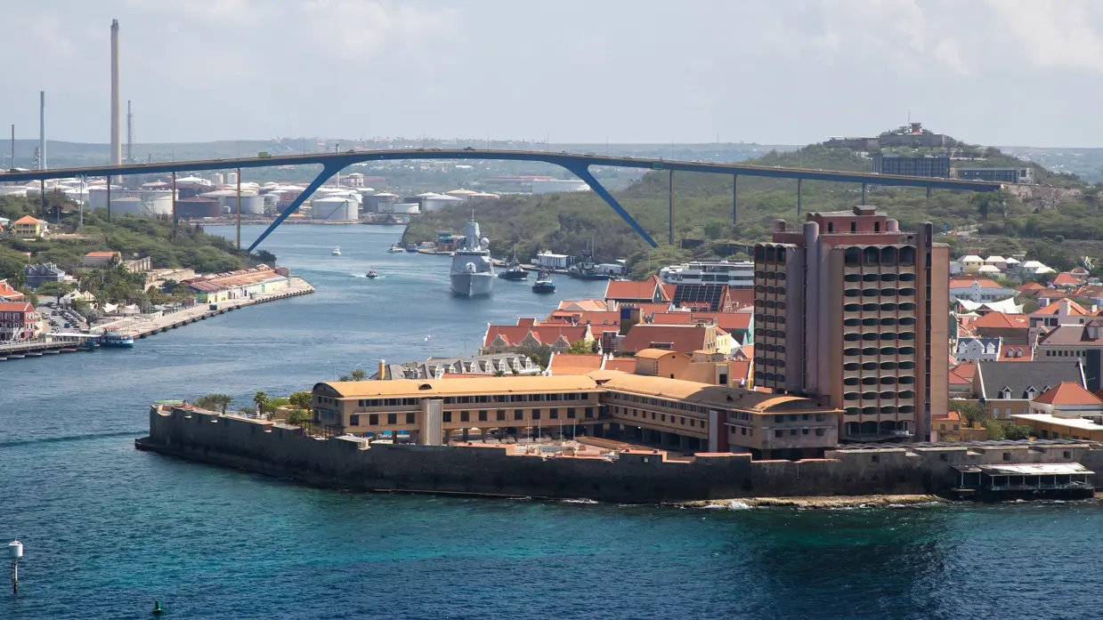 : Foto van Willemstad op Curaçao vanuit de lucht. In het midden 2 marineschepen.