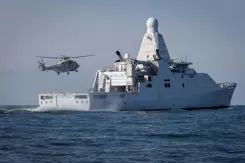 Marineschip Zr.Ms. Groningen op zee. Erboven vliegt een NH90 maritieme gevechtshelikopter.