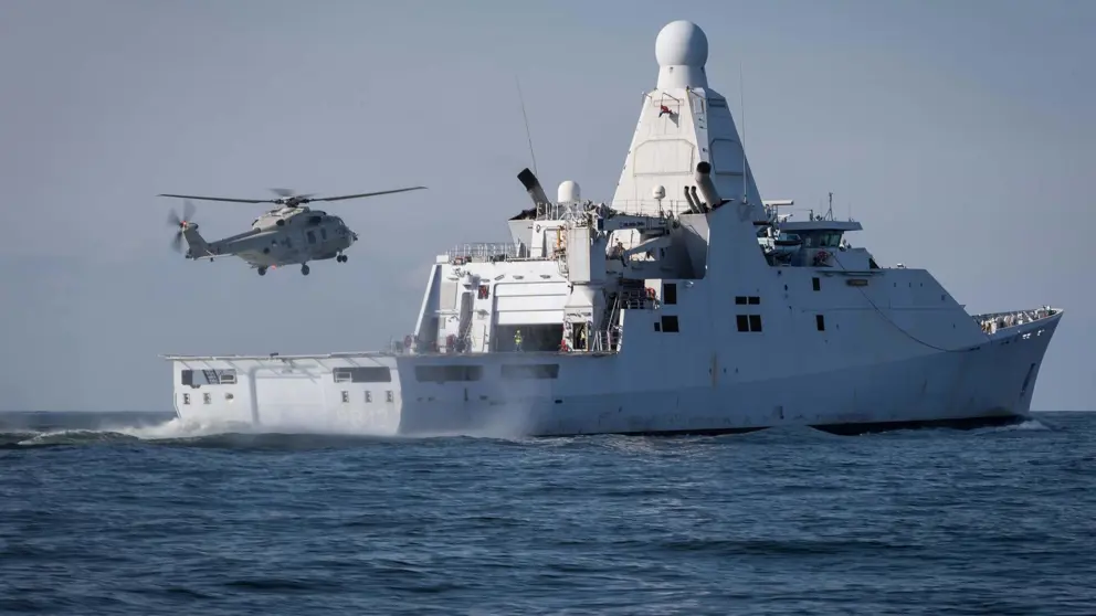 Marineschip Zr.Ms. Groningen op zee. Erboven vliegt een NH90 maritieme gevechtshelikopter.