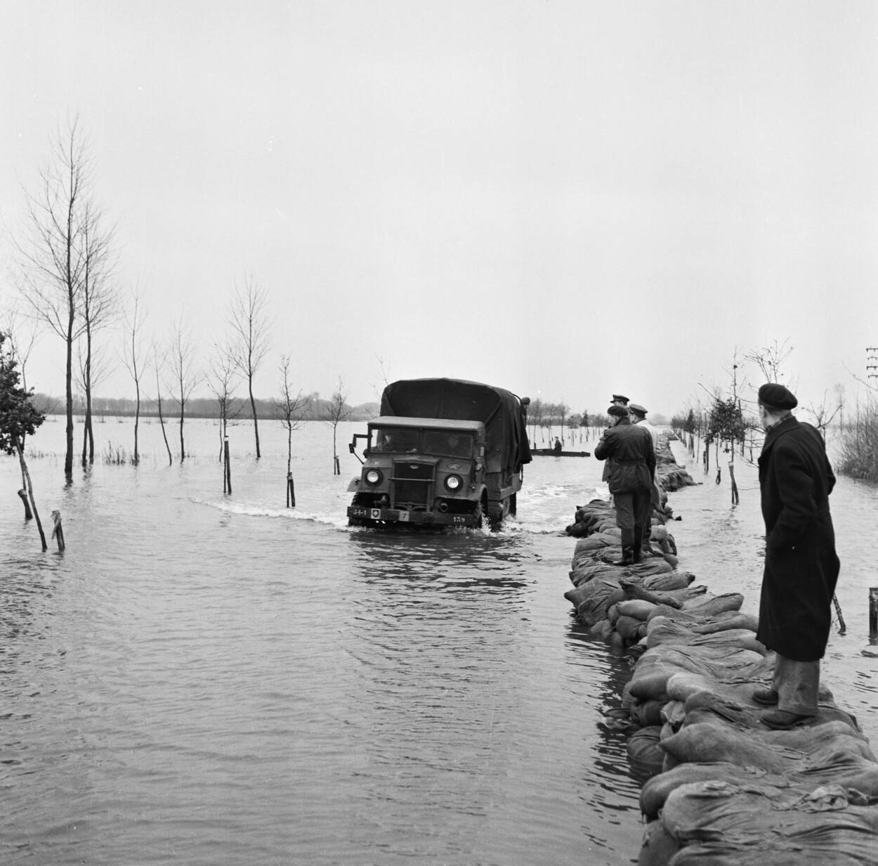 Een militaire vrachtauto (Chevrolet, 3-tonner, 4x4) rijdt langs een zandzakken-dijk tijdens reddingswerkzaamheden.