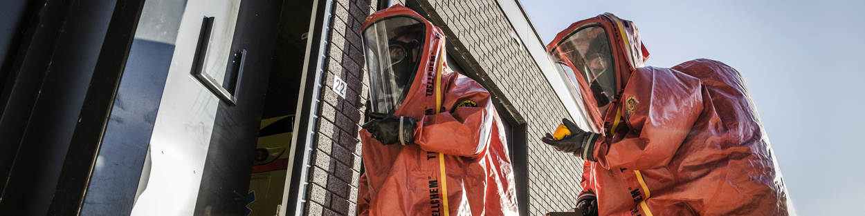 2 personen in beschermende kleding gaan een gebouw binnen.