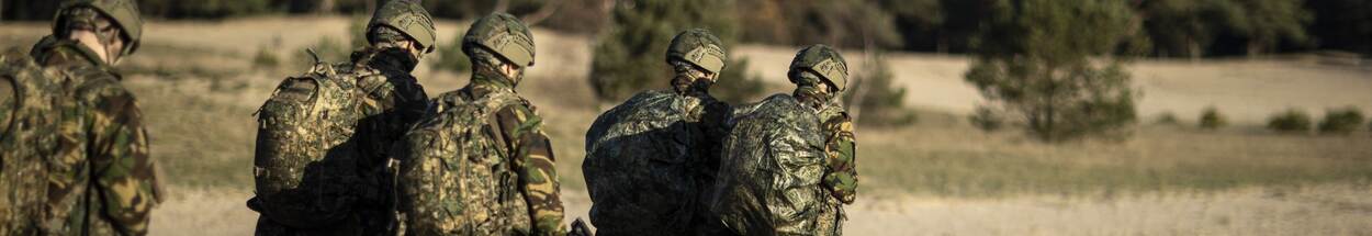 Militairen lopen op heide bij bos.