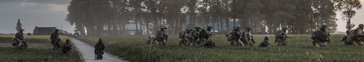 Militairen met bepakking lopen door het gras.