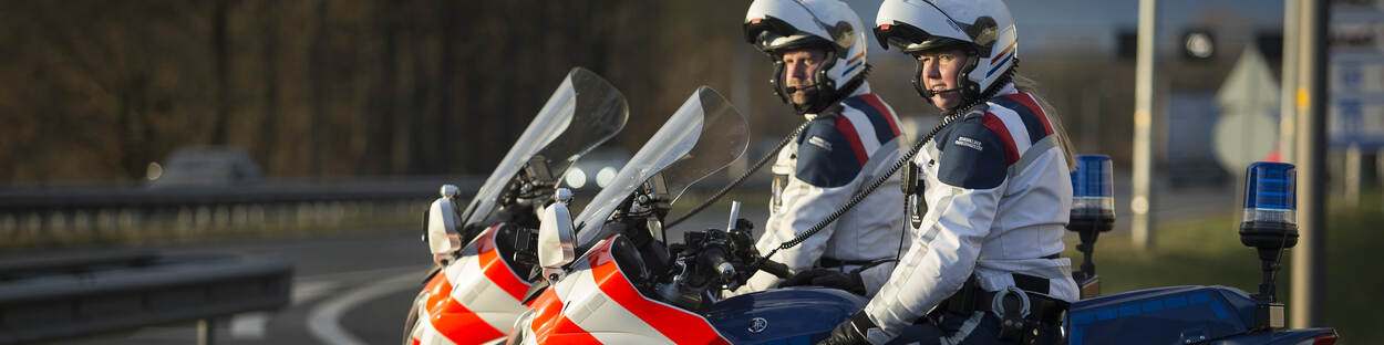 2 marechaussees op de motor staan langs de snelweg te surveilleren.