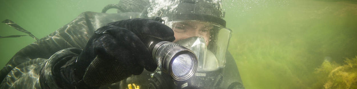 Defensieduiker met zaklamp onder water.