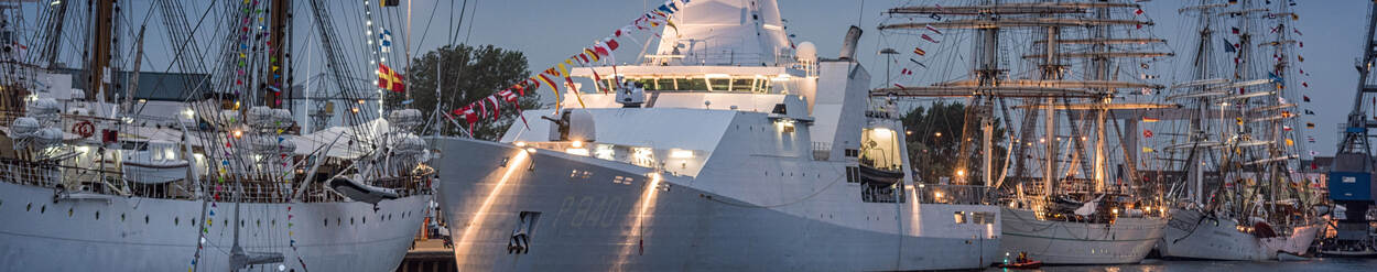 Sail-schepen en marineschip samen aan wal met verlichting.