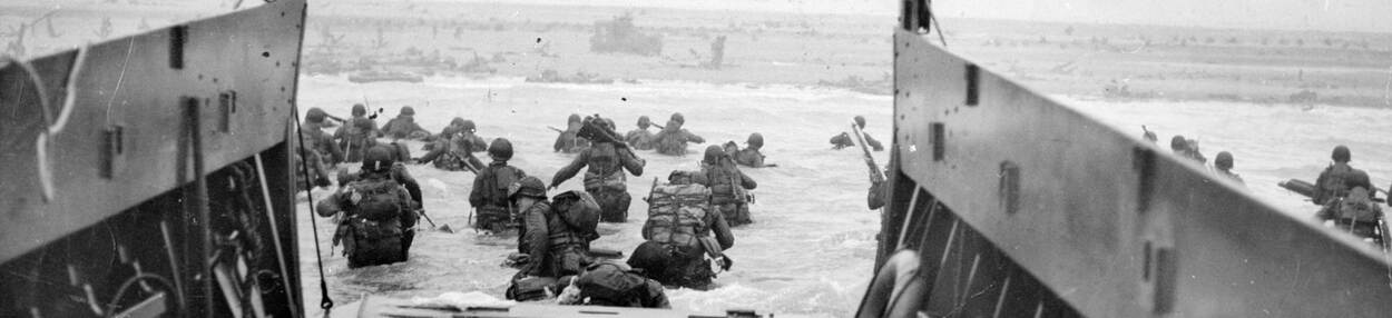 Zwart-witfoto van Amerikaanse militairen die vanuit landingsvaartuig waden naar Omaha Beach, Normandië.