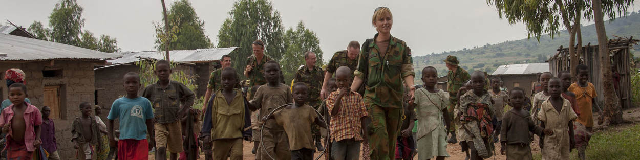 Nederlandse militairen lopen met kinderen over zandweg in missiegebied.