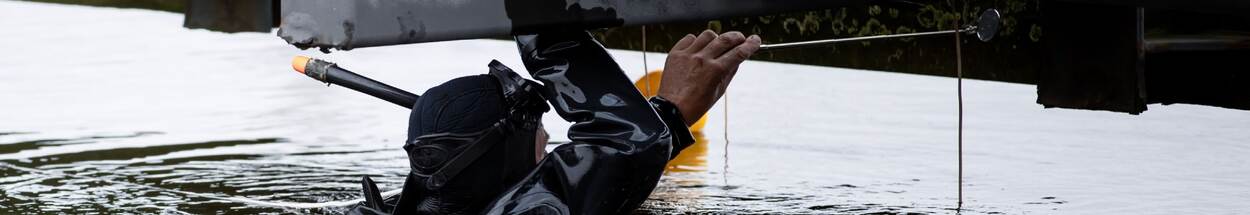 Een duiker onderzoekt explosieven bij schip, aan wateroppervlak.