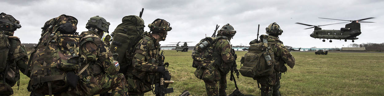 Militairen met bepakking kijken naar een landende Chinook.