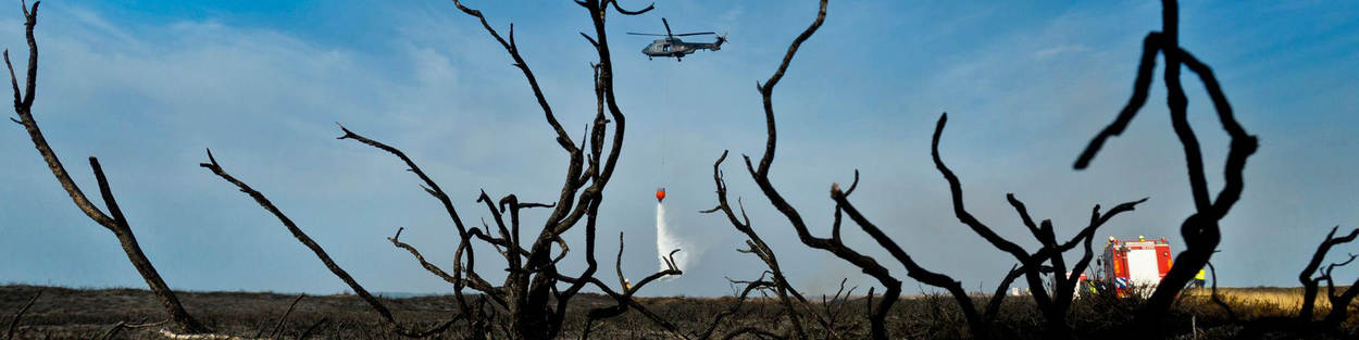 Helikopter met daaronder een bambi bucket bestrijdt een brand.