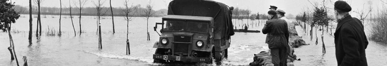 Een militaire vrachtauto (Chevrolet, 3 ton, 4x4) rijdt langs een zandzakken-dijk tijdens reddingswerkzaamheden na de overstroming in 1953.