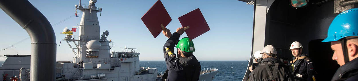Militair houdt gekleurde borden in de lucht om te communiceren met ander schip.