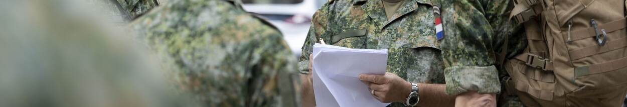 Militair met papier in hand, omringt door andere militairen.