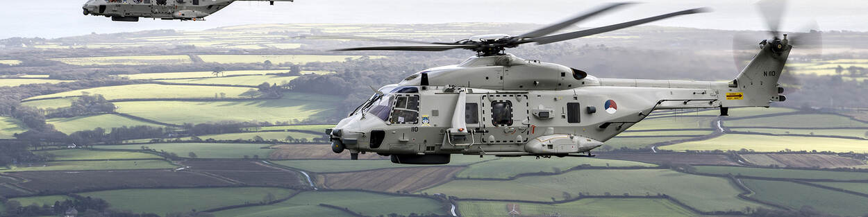 Twee helikopters vliegen boven groene weilanden