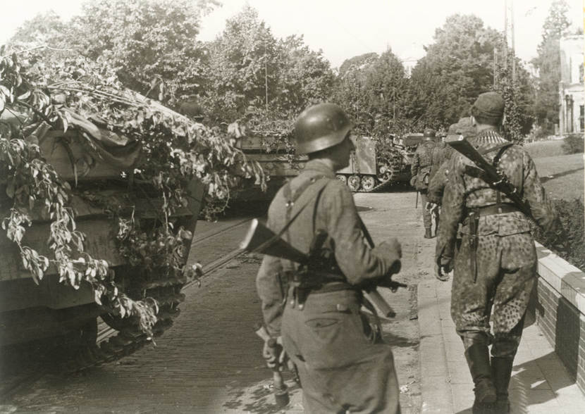 Historische zwart-witfoto van zwaarbewapende SS'ers naast pantservoertuigen en tanks tijdens Market Garden.