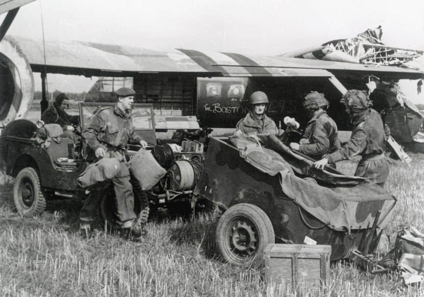 Historische zwart-wit foto van geallieerde militairen die zich voorbereiden op Market Garden. Op de achtergrond een Airspeed Horsa zweefvliegtuig waarmee ze zullen worden.