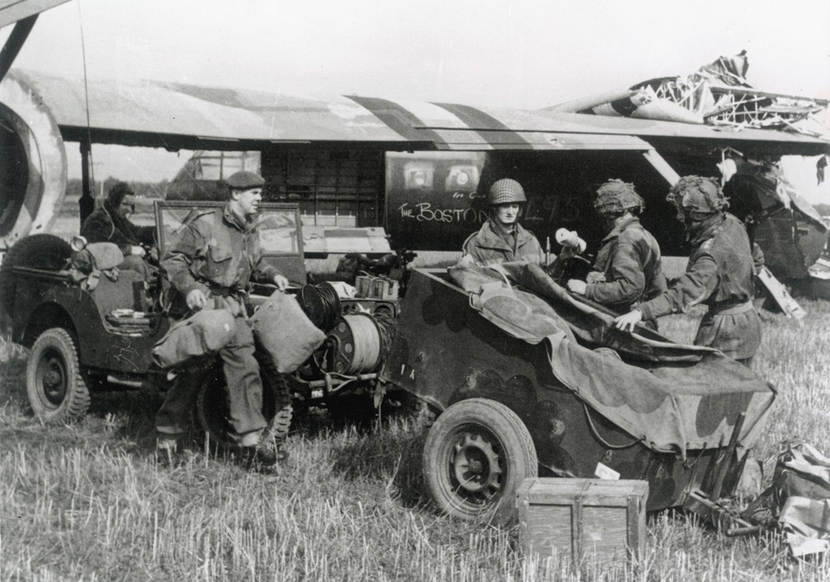 Zwart-wit foto van geallieerde militairen met voertuigen. Achter hen een Airspeed Horsa-zweefvliegtuig.