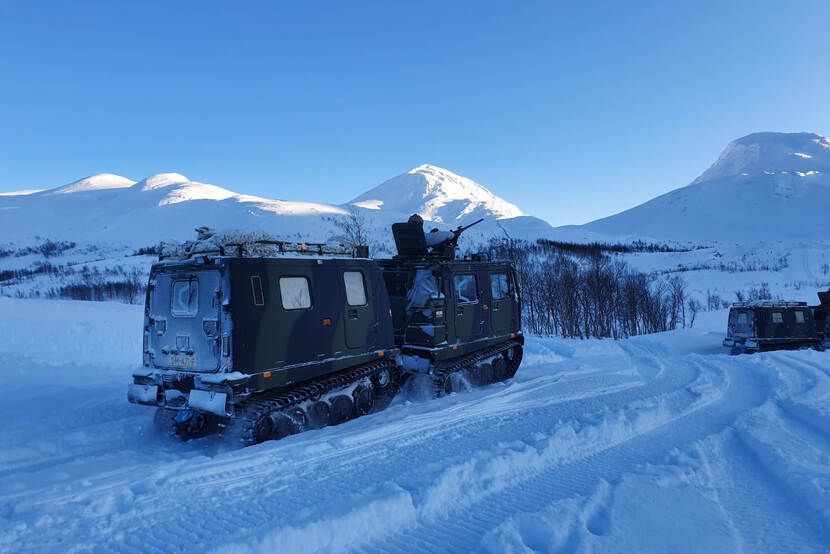 Een militair voertuig rijdt door sneeuwlandschap.