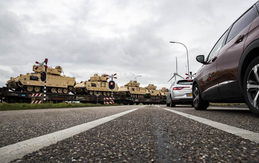 Amerikaanse tanks verplaatsten zich per spoor, rij auto's wacht voor spoorwegovergang.
