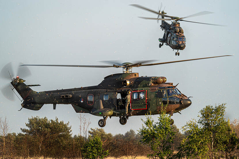 2 Defensie-helikopters vliegen laag boven bomen.