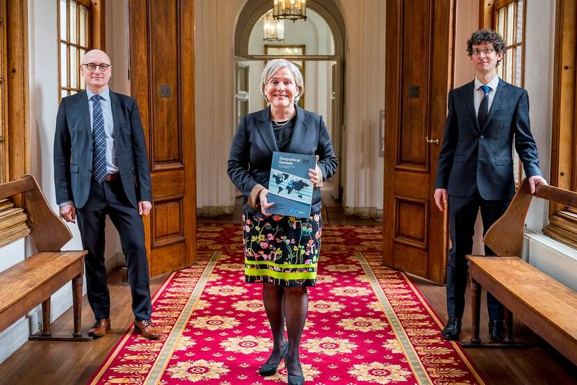De minister poseert met boek in de hand tussen 2 wetenschappers.