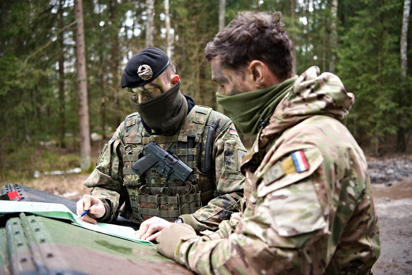 2 militairen in het bos overleggen, kijkend op een kaart.