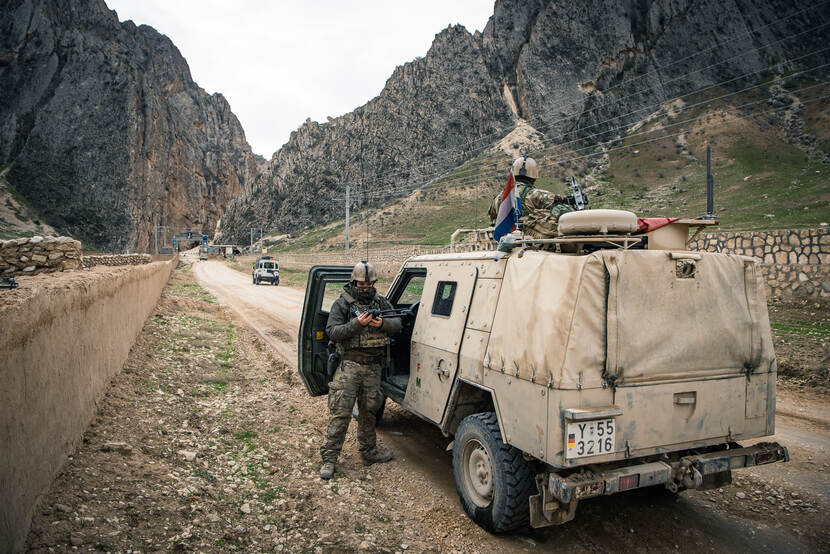 Een militair staat naast een stilstaand militair voertuig in de bergen.