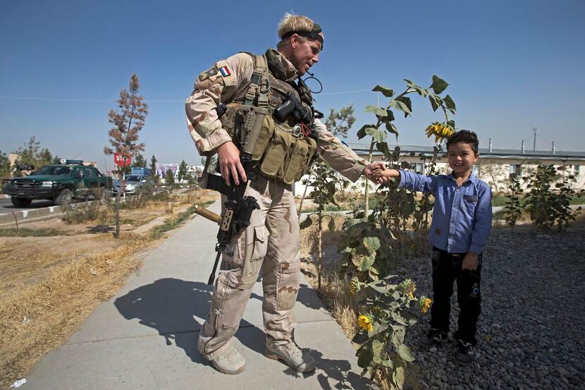 Militair en Afghaans jongetje geven elkaar een hand.