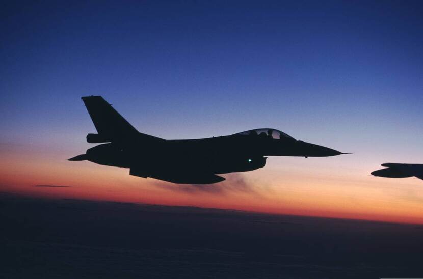 Vliegende F-16 tegen een avondrode lucht.