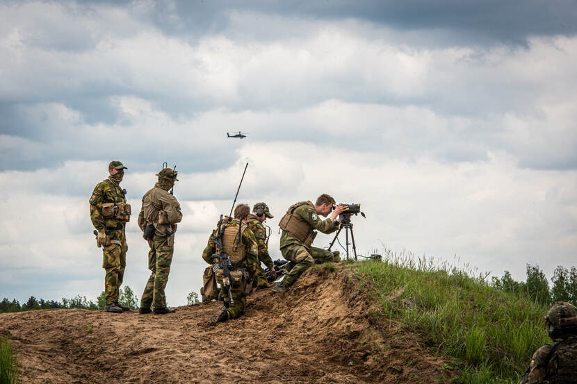 Noorse militairen en een Duitse die samen Nederlandse militairen meedoen aan Iron Wolf. Met een kijker op een onderstel wordt de omgeving in de gaten gehouden.