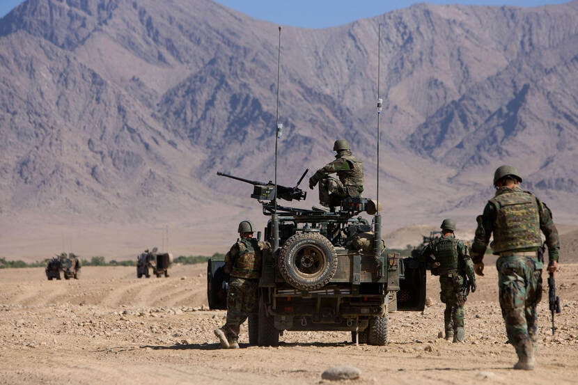 Patrouille van militairen met jeep over een zandvlakte in Afghanistan,op de achtergrond hoge bergen.