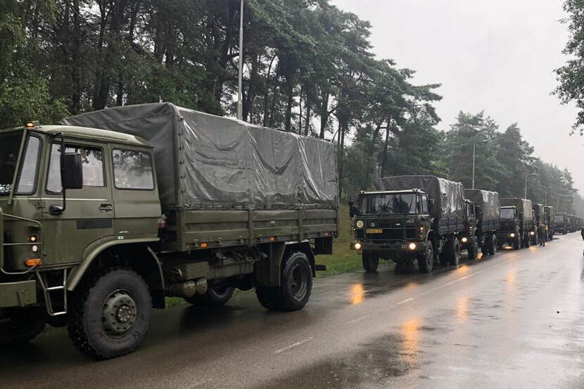 Colonne militaire voertuigen in de regen in bosrijk gebied.