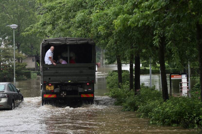Militair voertuig met inwoners van Valkenburg rijdt over een overstroomde weg.