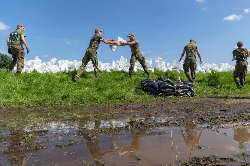 Militairen op een dijk geven zandzakken aan elkaar door.