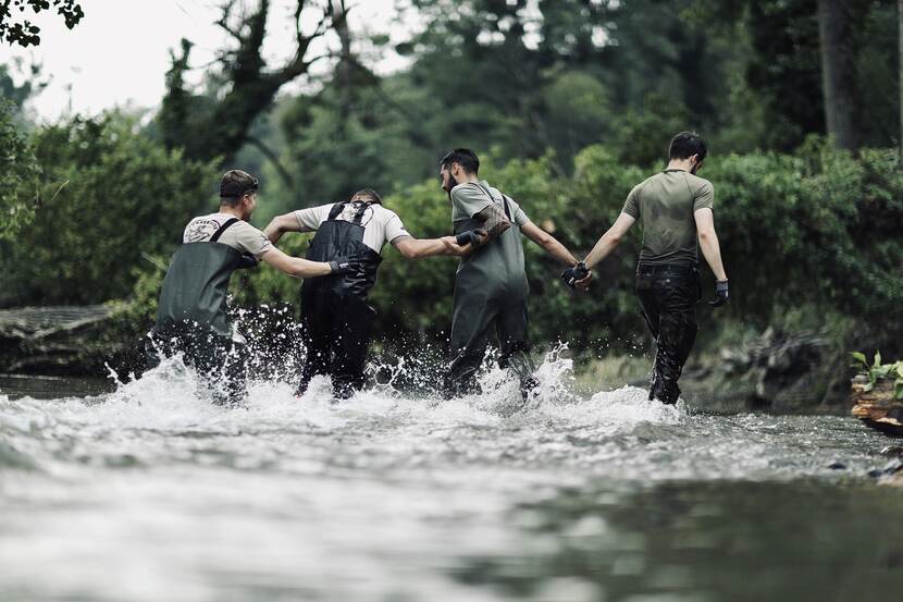 Militairen helpen elkaar door het water.