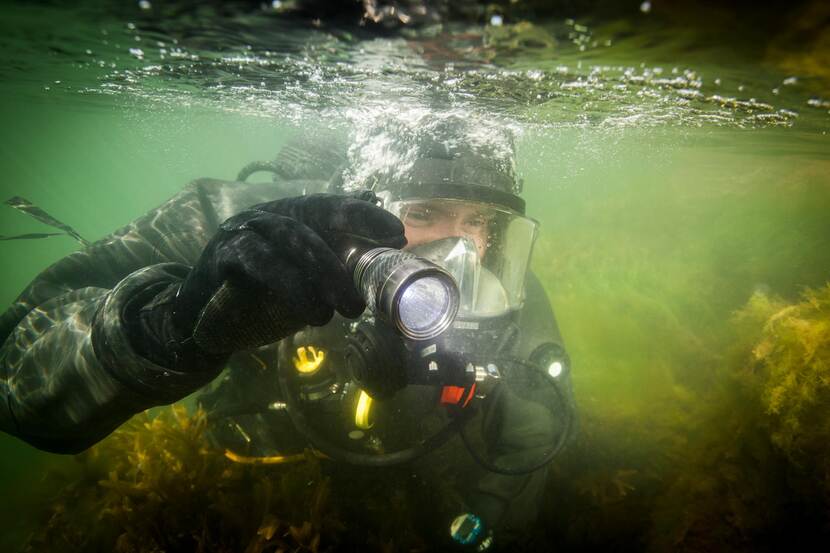 Militaire duiker met zaklamp onder water.