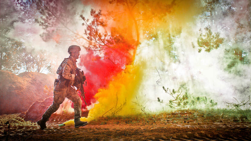 Een militair van de eFP in Litouwen rent tegen de achtergrond van oranje rook van een rookgranaat.