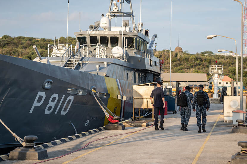 Patrouilleboot Jaguar van de Kustwacht Caribisch Gebied ligt aangemeerd in de haven. 3 militairen lopen erlangs.