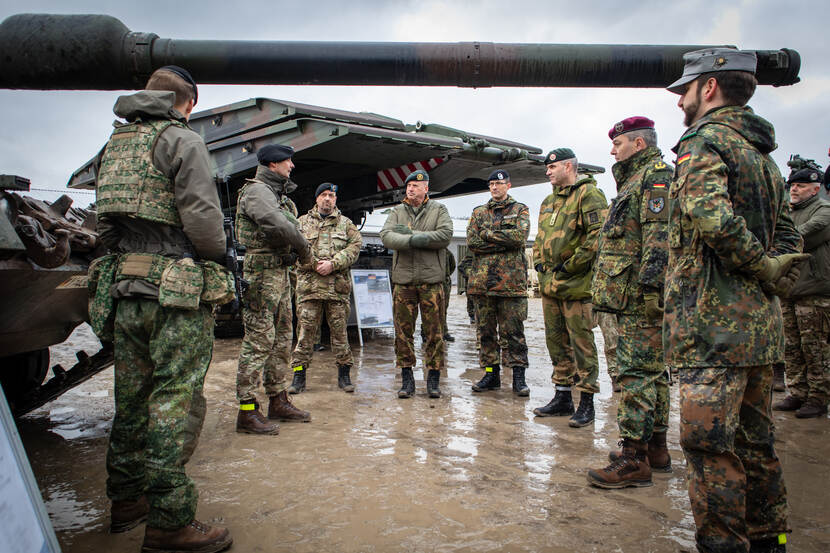 Commandanten landstrijdkrachten bezoeken militairen in Litouwen. Staan in kring tussen voertuigen.