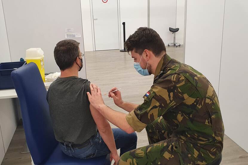 Een militair vaccineert een jonge man.