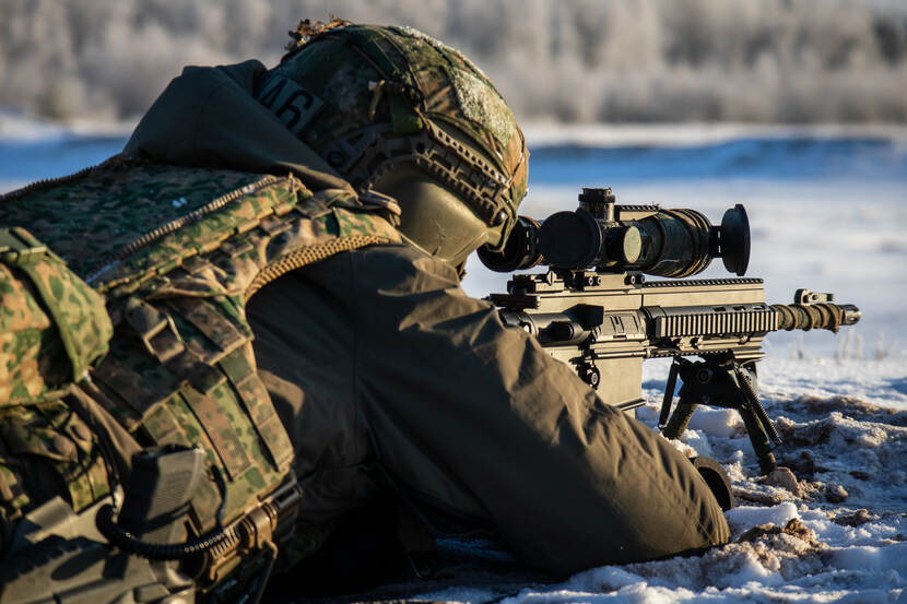 Een militair ligt in de sneeuw en kijkt door het vizier van zijn schietwapen.