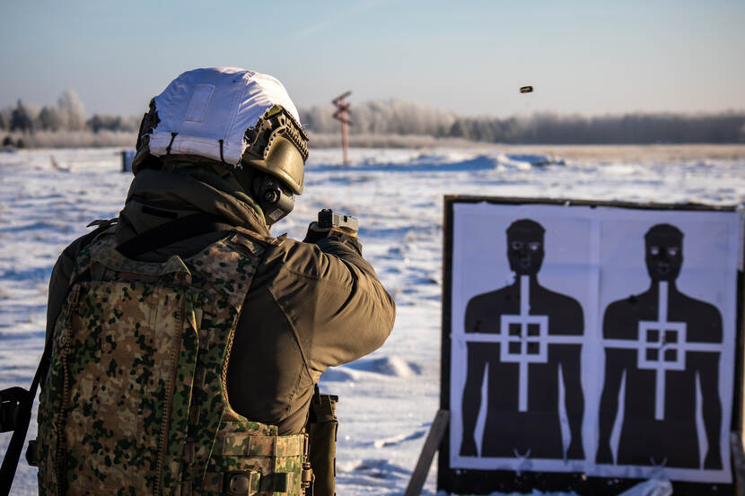 Een militair in besneeuwd landschap richt zijn wapen op een houten bord, met daarop persoonssilhouetten op papier.