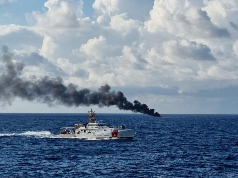 Schip Kustwacht Caribisch Gebied op zee, met op de achtergrond het brandend smokkelvaartuig.
