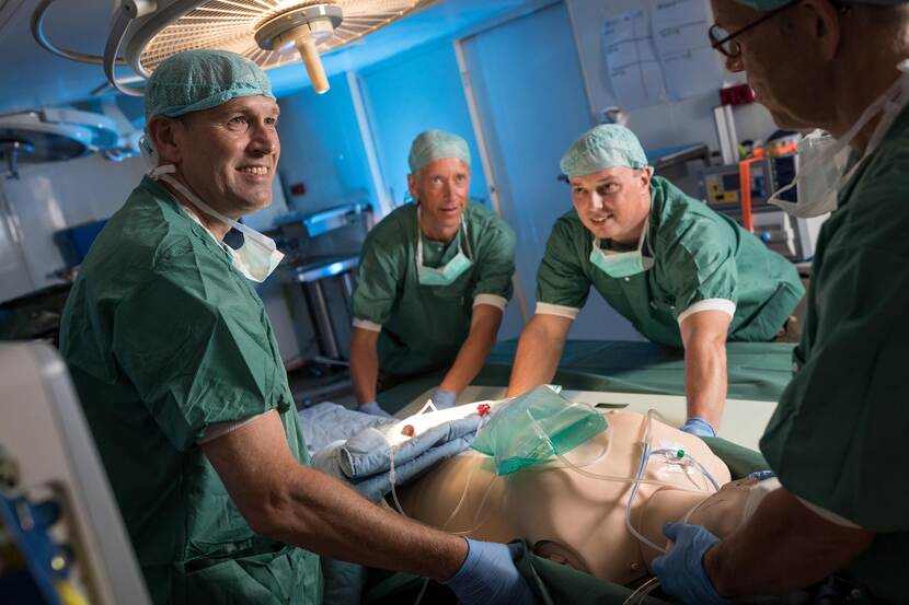 Een chirurgisch team tilt een oefenpop op een operatietafel.