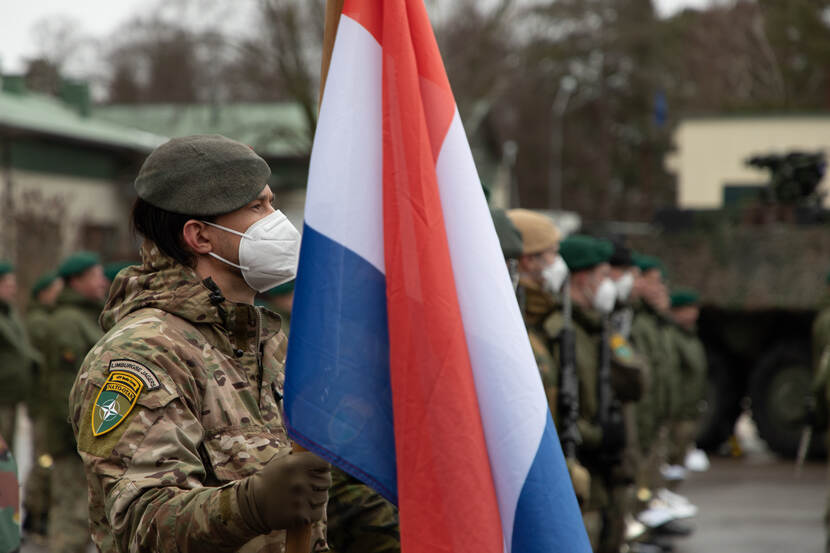 Militairen met mondkap op een rij, de 1e draagt de Nederlandse vlag.